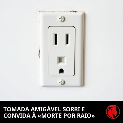 Uma tomada elétrica de parede americana, de receptáculo único, cujas fendas e furo de aterramento lembram um rosto amigável e sorridente. Legenda: Tomada amigável sorri, convida para a 'Morte por Raio'.